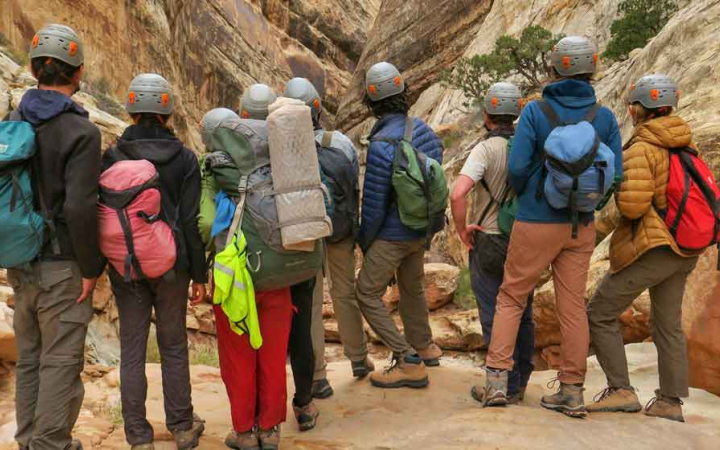 A group of students wearing helmets face away from the camera looking into a canyon